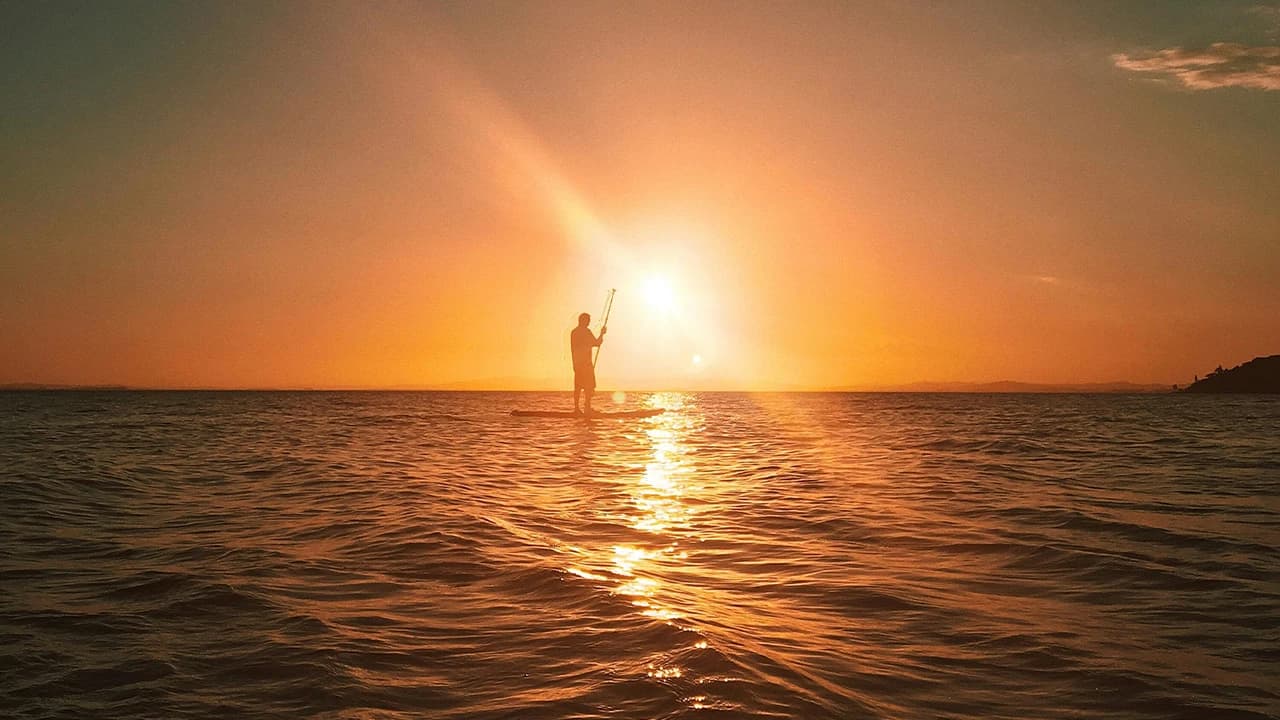 Silhouette of a paddleboarder at golden sunset on calm Maldives waters